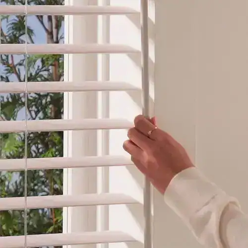 Bright white window blinds being adjusted by hand, showcasing premium window treatment options from Blinds West. Perfect for sunlight control and home decor.