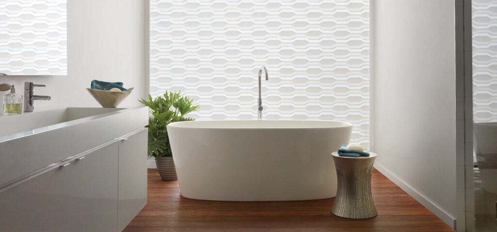 Contemporary free-standing bathtub in a modern bathroom with sleek white walls and textured window treatments, highlighting luxury bathroom design and custom window coverings by Blinds West.