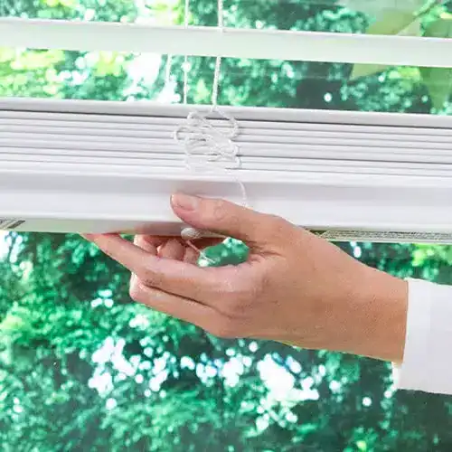 Adjusting white window blinds with a hand, showcasing high-quality window treatments from Blinds West.