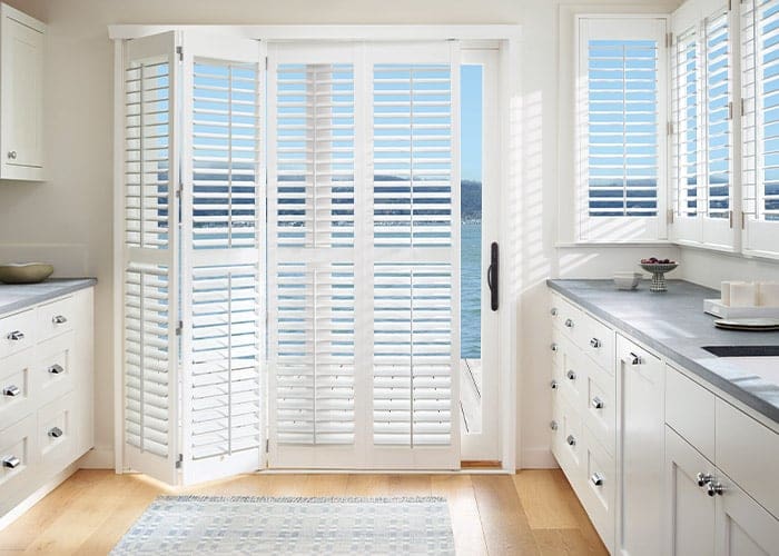 Custom white plantation shutters on sliding glass doors for enhanced privacy and light control in kitchens. Perfect window treatment solution from Blinds West.