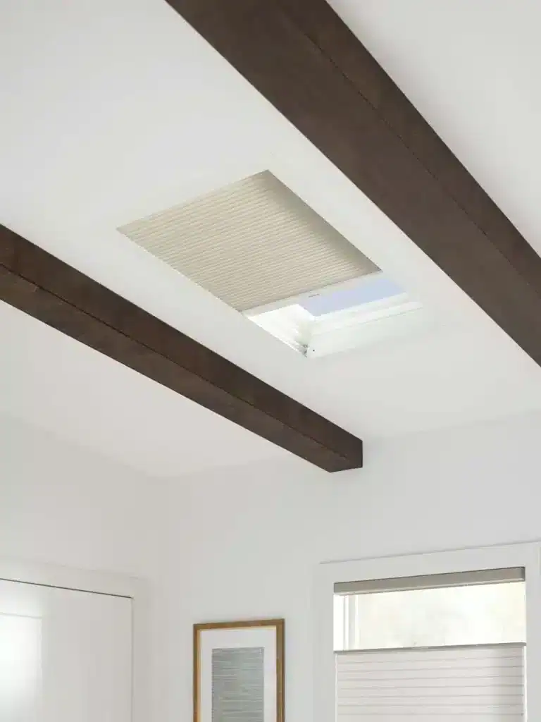 Ceiling skylight with black beams and a beige window shade in a modern home.