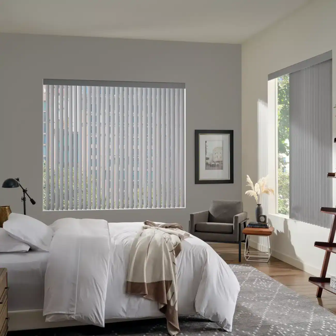 Modern bedroom with large windows featuring white vertical blinds, cozy bed, stylish furniture, and natural light, showcasing custom drapery solutions by Blinds West.