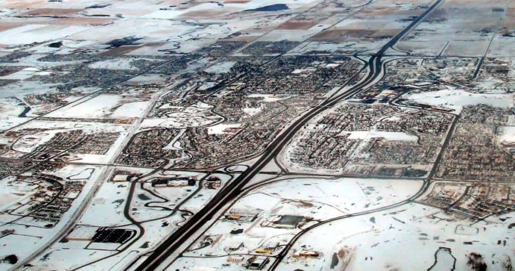 Aerial view of a snowy cityscape showing highways and neighborhoods covered in snow, highlighting urban planning and winter weather conditions.